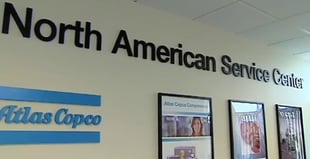 Picture of a wall with Atlas Copco logo and pictures of employees.