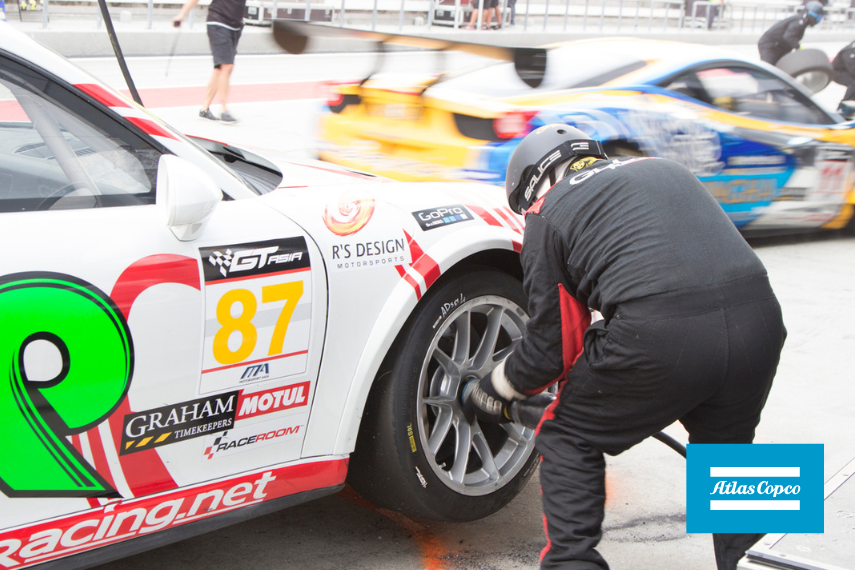 Pit crew with pneumatic tools putting a tire on car