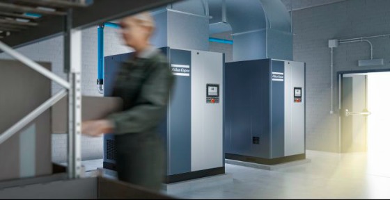Image of someone walking past two Atlas Copco air compressors