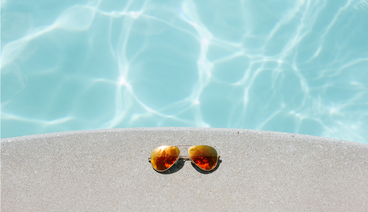 Picture of aviator-sunglasses by the edge of a pool with clear sun-lit water